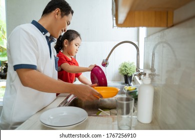 Asian Daughter Helping Her Father In The Kitchen Washing Dishes Together