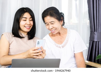 Asian Daughter With Old Mother Using Mobile Phone And Laptop Sharing Technology Together 