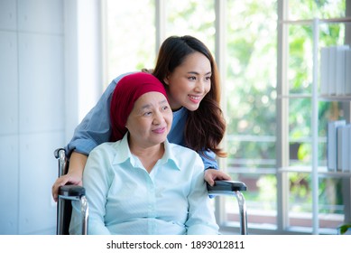 Asian daughter stand closely to her mother who sitting on wheelchair and wearing red headscarf smiling and looking through window with feeling happy.  Cancer or leukemia survivor concept. - Shutterstock ID 1893012811