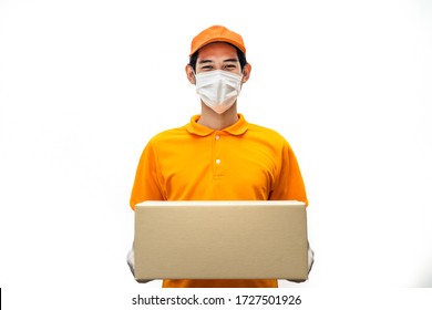 Asian deliver man wearing face mask in orange uniform holding box of food, groceries, things standing in white isolated background. Postman and express grocery delivery service during covid19 pandemic