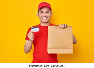 Asian Delivery Employee Man In Red T-shirt Work Courier Service From Shop Restaurant To Home Office Hold Credit Bank Card Brown Craft Paper Takeaway Food Bag Mockup Isolated Over Yellow Background