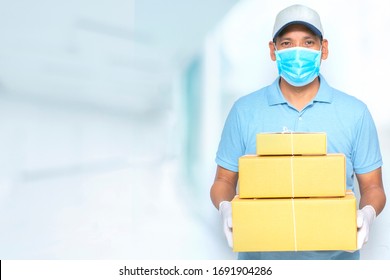 Asian Delivery Man  In Blue Cap And Blank Blue Uniform With Face Mask Gloves Hold Empty Cardboard Box On Blur Modern Room Background,  Quarantine Pandemic Corona Virus Or Covid-19.shopping Online