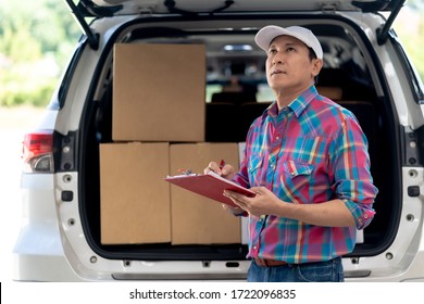 Asian Delivery Man checking list on clipboard near a Car. Senior  Delivery Man holding in documents on clipboard Check Box.
