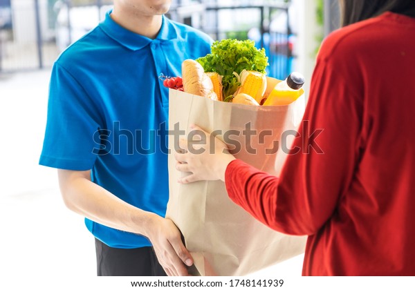 Asian delivery man delivering food, fruit, juice
and vegetable to customer home - online grocery shopping service
concept