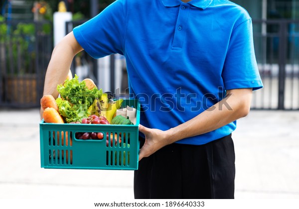 Asian delivery man delivering food, fruit, juice\
and vegetable to customer home - online grocery shopping service\
concept