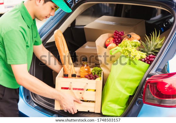 Asian delivery man grocery prepare service giving\
fresh vegetables food and fruit full in wooden basket on back car\
to send woman customer at door home after pandemic coronavirus,\
Back to new normal