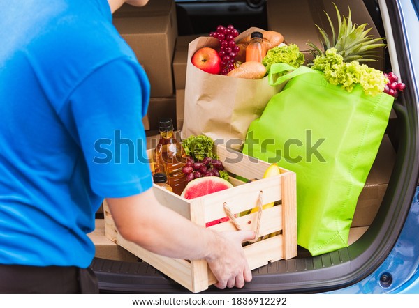 Asian delivery man grocery prepare service giving\
fresh vegetables food and fruit full in wooden basket on back car\
to send woman customer at door home after pandemic coronavirus,\
Back to new normal