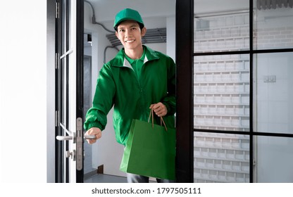 Asian Delivery Man Holding Shopping Paper Bag And Opening Door For Send Product To Customer By Quality Express Service While Wearing Green Jacket Uniform With Cap At Company Office