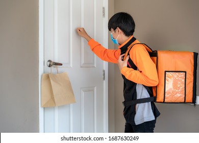 Asian delivery man send food bag at door knob for contactless or contact free from delivery rider in front house for social distancing for infection risk.