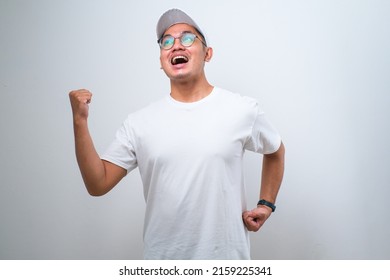 Asian delivery man wearing cap standing over isolated white background very happy and excited doing winner gesture with arms raised, smiling and screaming for success. Celebration concept.