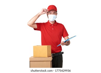 Asian Delivery Man Wearing Face Mask In Red Uniform Standing With Parcel Post Box Isolated Over White Background. Express Delivery Service During Covid19.