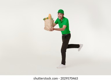 Asian Delivery Man Wearing In Green Uniform Holding Fresh Food Paper Bag And Running Isolated Over White Background.	Express Delivery Concept.