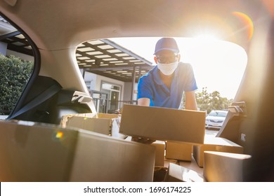 Asian Delivery man wearing mask picking up the package on front receiver shipping deliver cargo social distancing, Many parcel in trunk hatchback car while the virus is spreading at sunset.