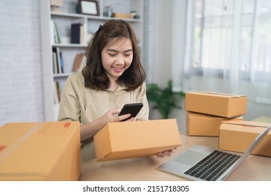 Asian Delivery Woman Freelance Worker Smiling Using Mobile Scan Barcode For Boxes For Sending Or Conveying Parcels By Mail. Work At Home.