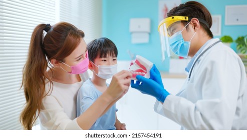 Asian Dentist With Face Shield And Mask Teach Boy How To Toothbrush Brushing Teeth Use Denture Model When Mother Sit By In Dental Clinic