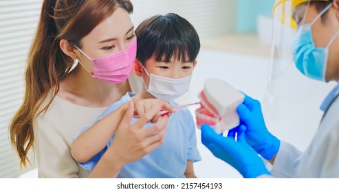 Asian Dentist With Face Shield And Mask Teach Boy How Use Toothbrush Brushing Teeth Use Denture Model When Mother Sit By In Dental Clinic - Kid Practice It