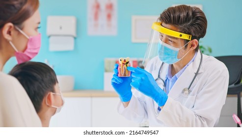 Asian Dentist With Face Shield And Mask Teach Boy Knowledge About Cavity With Teeth Model