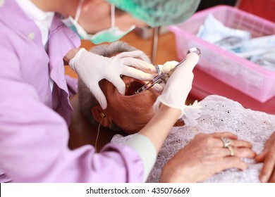 A asian dentist working on  elderly woman's teeth,dentist holding a syringe and anesthetizing his patient - Shutterstock ID 435076669