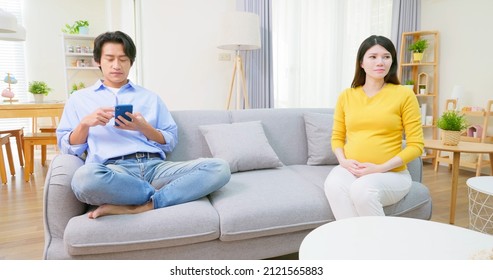 Asian Depressed Pregnant Woman Sitting On Couch Have Argument With Husband - Man Use Mobile Phone In Living Room At Home