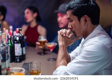 Asian depression man feeling heart broken and drinking beer in a bar. Attractive male sitting on counter bar, holding a bottle of alcohol feeling loneliness, drunk and hangover alone at night club. - Powered by Shutterstock