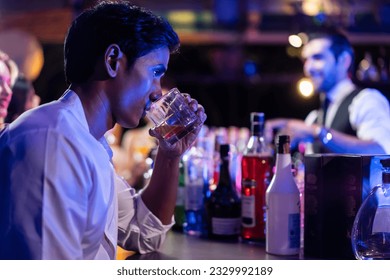 Asian depression man feeling heart broken and drinking beer in a bar. Attractive male sitting on counter bar, holding a bottle of alcohol feeling loneliness, drunk and hangover alone at night club. - Powered by Shutterstock