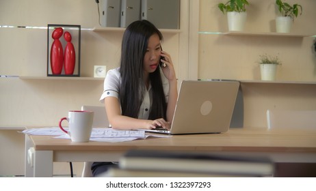 Asian designer talking on smartphone with client in the office. check information on computer. - Shutterstock ID 1322397293