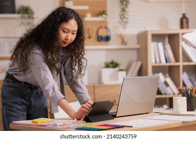 Asian Designer woman work from home and communicate with the design team over the internet. On a tablet,women are having a video conference call. - Shutterstock ID 2140243759