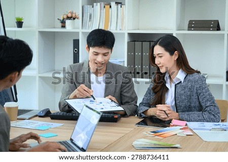 Asian developer team collaborates on UX UI app design, reviewing data charts and color palettes at a bright office table, ideal for tech and business concepts.