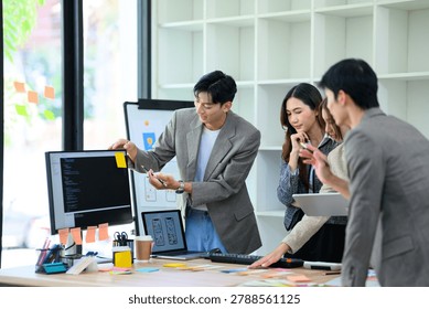 Asian developer team collaborating on UX UI app design, reviewing code and wireframes during a creative brainstorming session in a bright office.