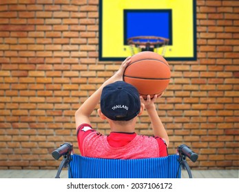 Asian Disabled Boy On Wheelchair Trying To Practice Basketball After Recovering From Fractured Ankle Injury In Front Yard Area At Home