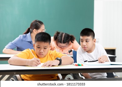 Asian Disabled Kids Or Autism Child Learning Looking And Writing At Desks In Classroom