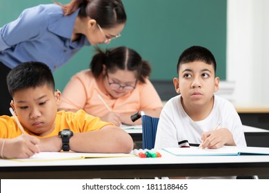 Asian Disabled Kids Or Autism Child Learning Looking And Writing At Desks With Teacher Helping In Classroom