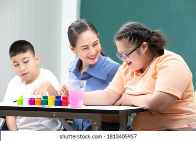 Asian Disabled Kids Or Autism Child Learning And Painting At Paper With Teacher Helping In Classroom