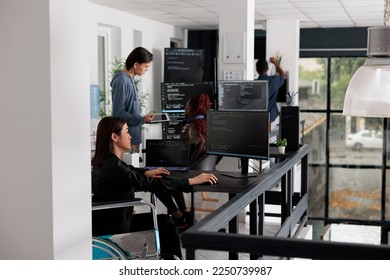 Asian disabled software programmer writing html code in agency big data room, using security system. Engineer with physical disability programming user interface artificial intelligence office.