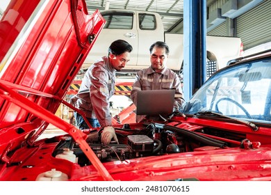 Asian diversity mechanic teamwork, Thai and Japanese car mechanic in grey uniforms. A man inspects the car engine with his assistant by a laptop. Automobile repairing service. Vehicle maintenance. - Powered by Shutterstock