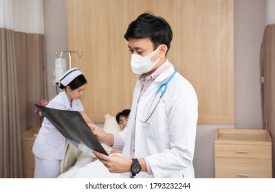 Asian Doctor With Face Mask Checking Lab Test Film X-ray Results Of Elderly Hospice Patient With Nurse At Hospital. People Health And Medical Concept.