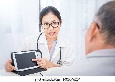  Asian Doctor Having Conversation With Her Senior Patient And Holding Ipad Gadget In Medical Office. Doctor Intern ( Woman ) Explaining X-ray Results To Patient