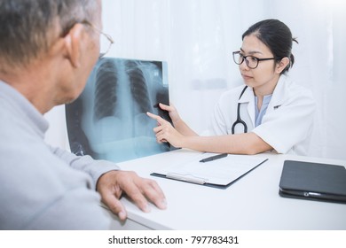 Asian Doctor Having Conversation With Her Patient And Holding Xray In Medical Office. Doctor ( Woman ) Explaining X-ray Results To Patient