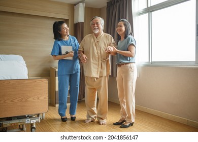 asian doctor helping old man patient walking in hospital with relative . senior male father and daughter with physical therapist