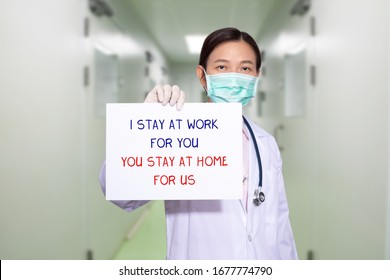 Asian Doctor At Hospital Wear Medical Masks, Holding Paper With Text I STAY AT WORK FOR YOU, YOU STAY AT HOME FOR US. Stay At Home Policy Campaign To Control COVID-19 Coronavirus Outbreak Situation