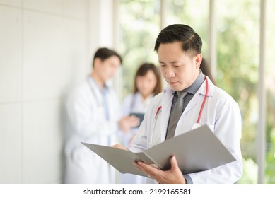 Asian Doctor Man Portrait In Professional Uniform Standing And Holding Folder To Review Data With Smile And Confidence.