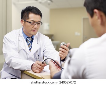 Asian Doctor Measuring Blood Pressure Of A Patient.