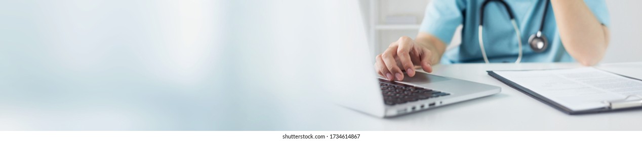 Asian Doctor or nurse in blue uniform concentrate working on laptop computer and preparing information of patients for meeting with medical team in hospital. Selective focus on hand. Banner, web