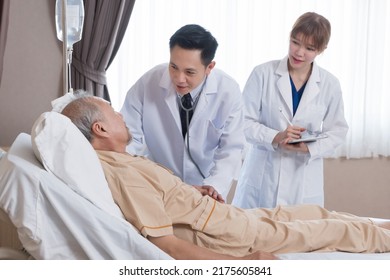 Asian doctor and nurse visit and take care senior man patient in room. Attractive two therapist practitioner explain diagnosis in hospital ward to treatment to elderly older male during appointment. - Shutterstock ID 2175605841