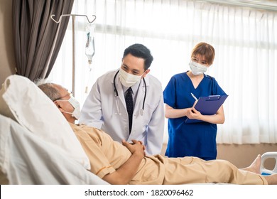 Asian Doctor And Nurse Wearing Mask Checking Health Of Senior Old Patient In Hospital Recovery Room. The Elder Man Infected Covid Lying On Bed Receiving Treatment And Diagnosis From Medical Team.