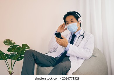 Asian Doctor or Physician Wear Face Mask Catch Headphone Use Smartphone or Mobile Phone to Check Patient Healthcare at Medical Office or Doctor Room in Vintage Tone