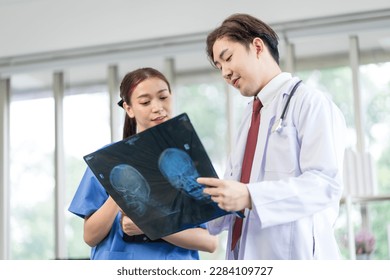 Asian doctor professionally examining a patient's x-ray to analyze the disease for the patient - Powered by Shutterstock