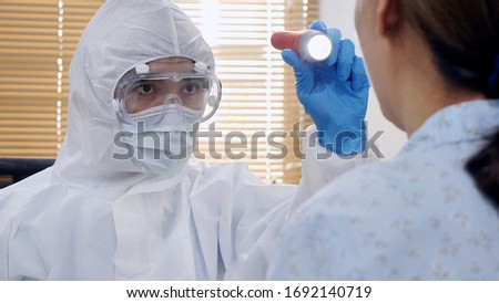 Asian doctor in protective PPE suit wearing face mask and eyeglasses using flash light examine the female patient's neck