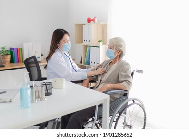 Asian doctor talk with old female patient about disease symptom, doctor use stethoscope listening lung of patient,   elderly health check up , they wear surgical mask on white background