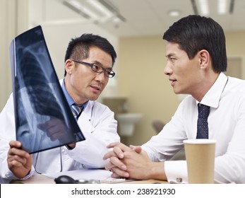 Asian Doctor Talking To Patient About X-ray Result.